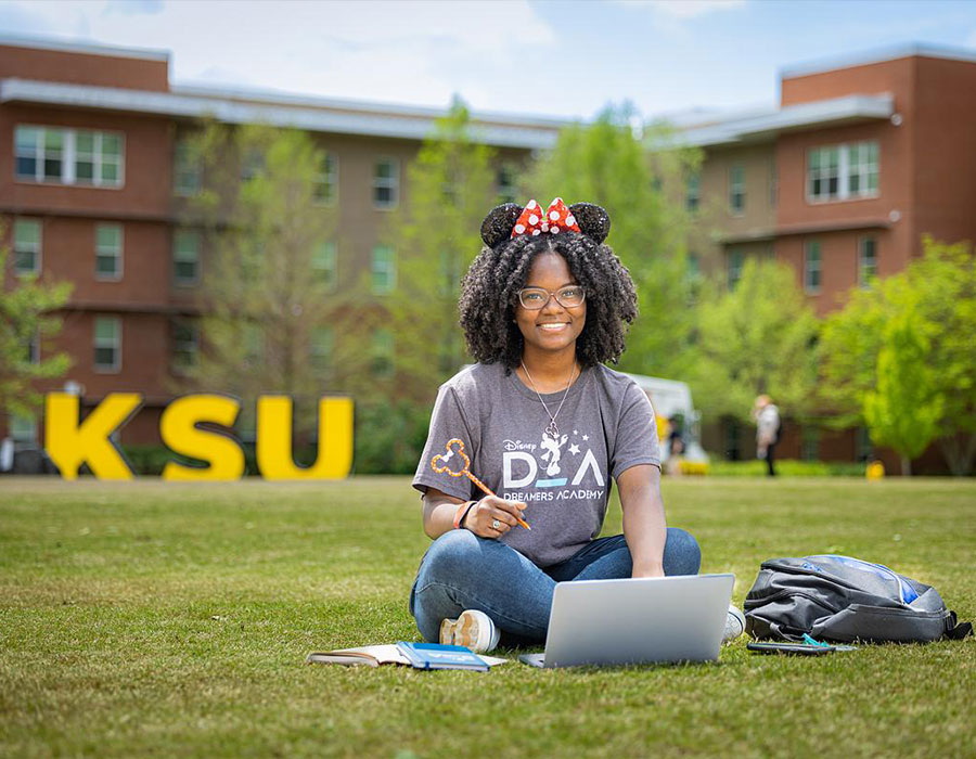 ksu student sitting on the campus green using their laptop.